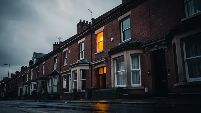 A handsome red-brick Victorian terraced house facade at dusk, one window lit warm, seen slightly from below.
